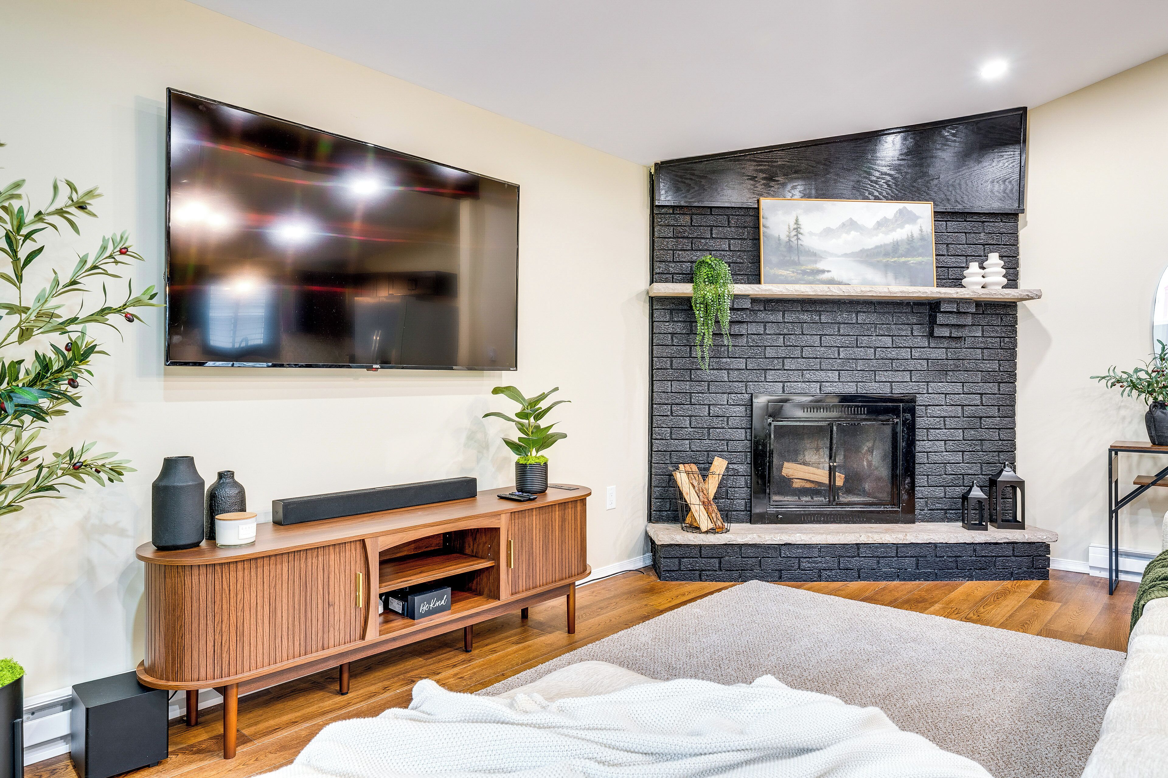 A modern living room with a flat-screen TV, a fireplace, a wooden entertainment unit, and a large plant.