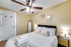 A hotel room with a bed, a ceiling fan, a nightstand with a lamp, and two framed pictures on the wall.