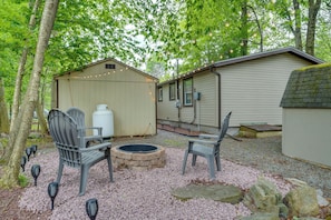 A covered outdoor seating area with chairs and a fire pit, surrounded by trees and a building with string lights. - Poconos Family Retreat w/ Fire Pit & Sunroom! (Tobyhanna)