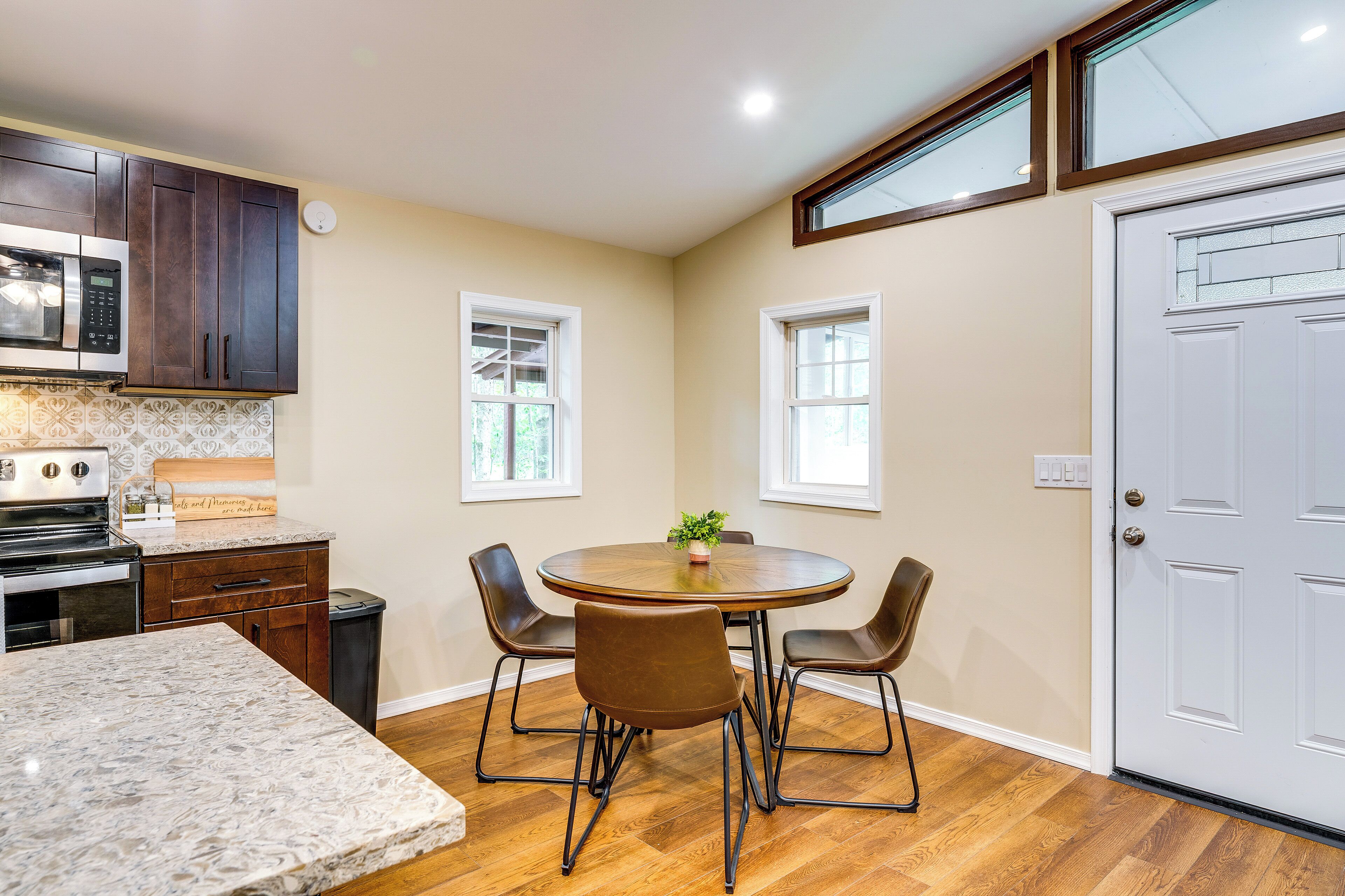A kitchen with a granite countertop, dark wooden cabinets, a microwave, and a dining area with a round table and chairs.