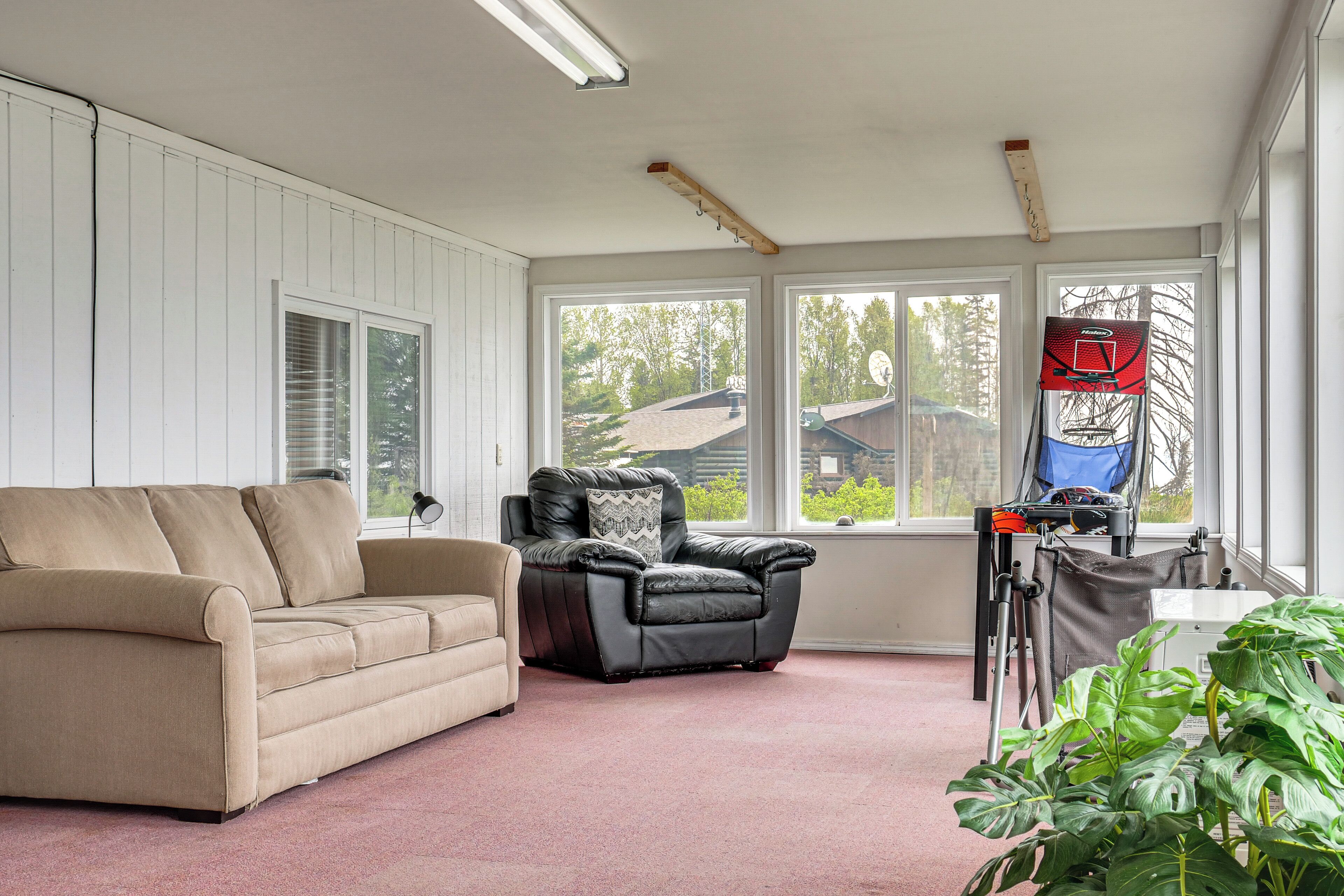 A room with a beige sofa, a black leather chair, a basketball hoop, and a large window.