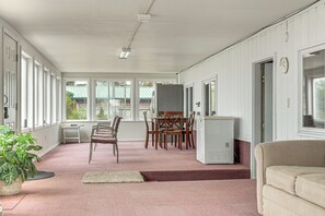 A room with a dining table, chairs, a refrigerator, a sofa, and a large window. - 6 Mi to Kenai Beach! Cozy Ocean-view Escape (Kenai)
