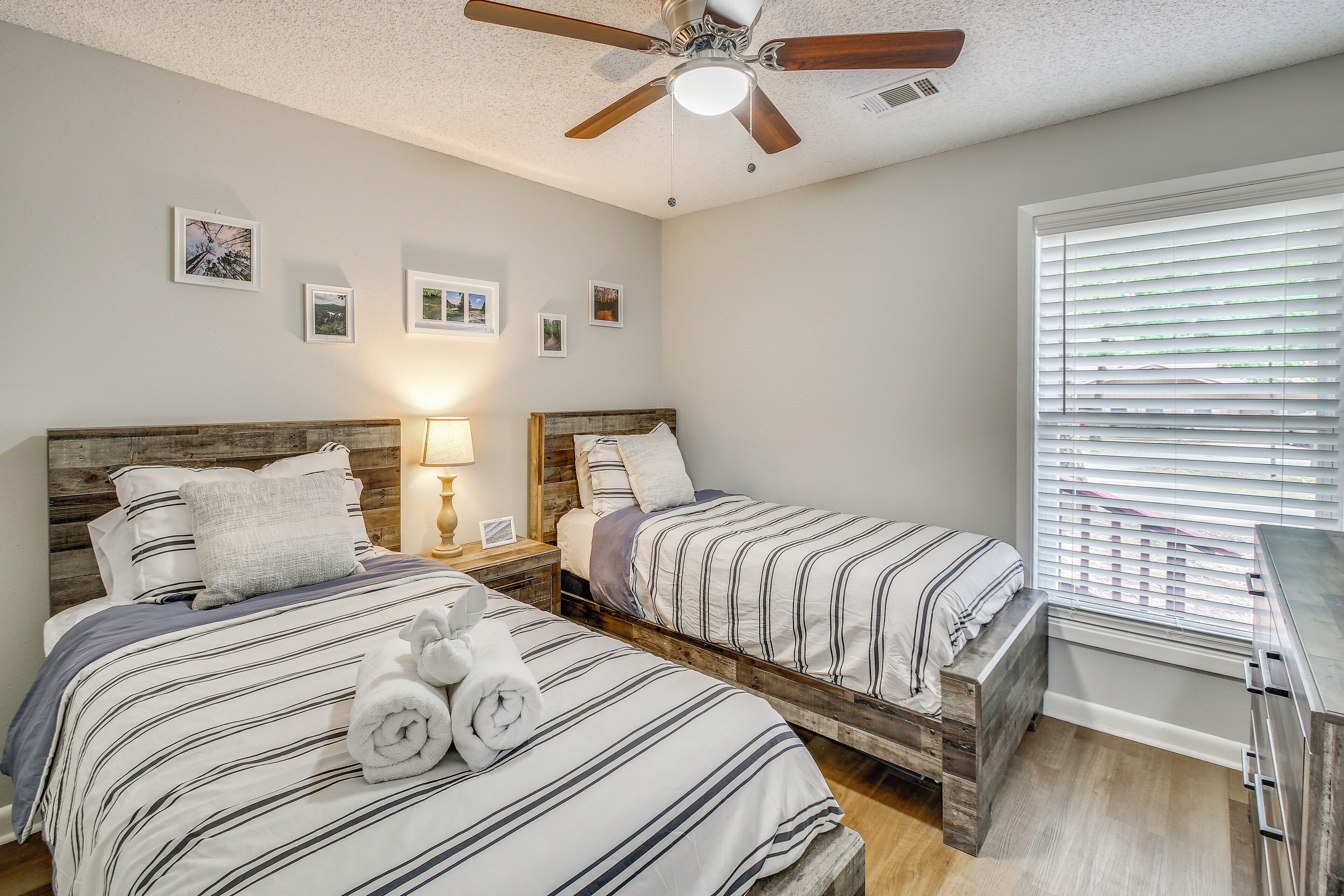 A bedroom with two beds, a ceiling fan, a nightstand with a lamp, and a window with blinds.