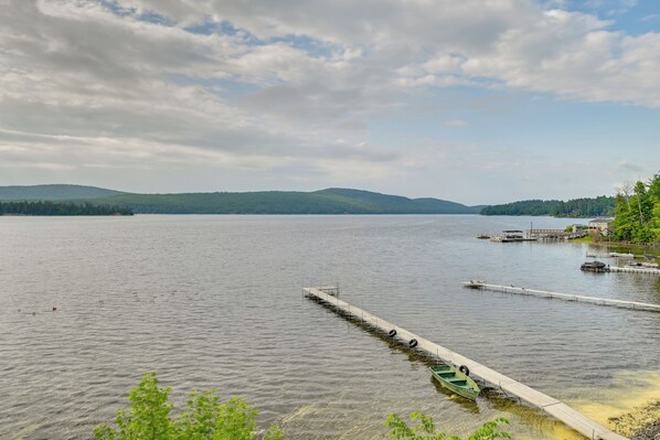 A calm lake with a wooden dock extending into the water, surrounded by greenery and distant hills.