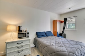 Un dormitorio con cama, una mesita de noche con lámpara, un microondas y una ventana con cortinas.
