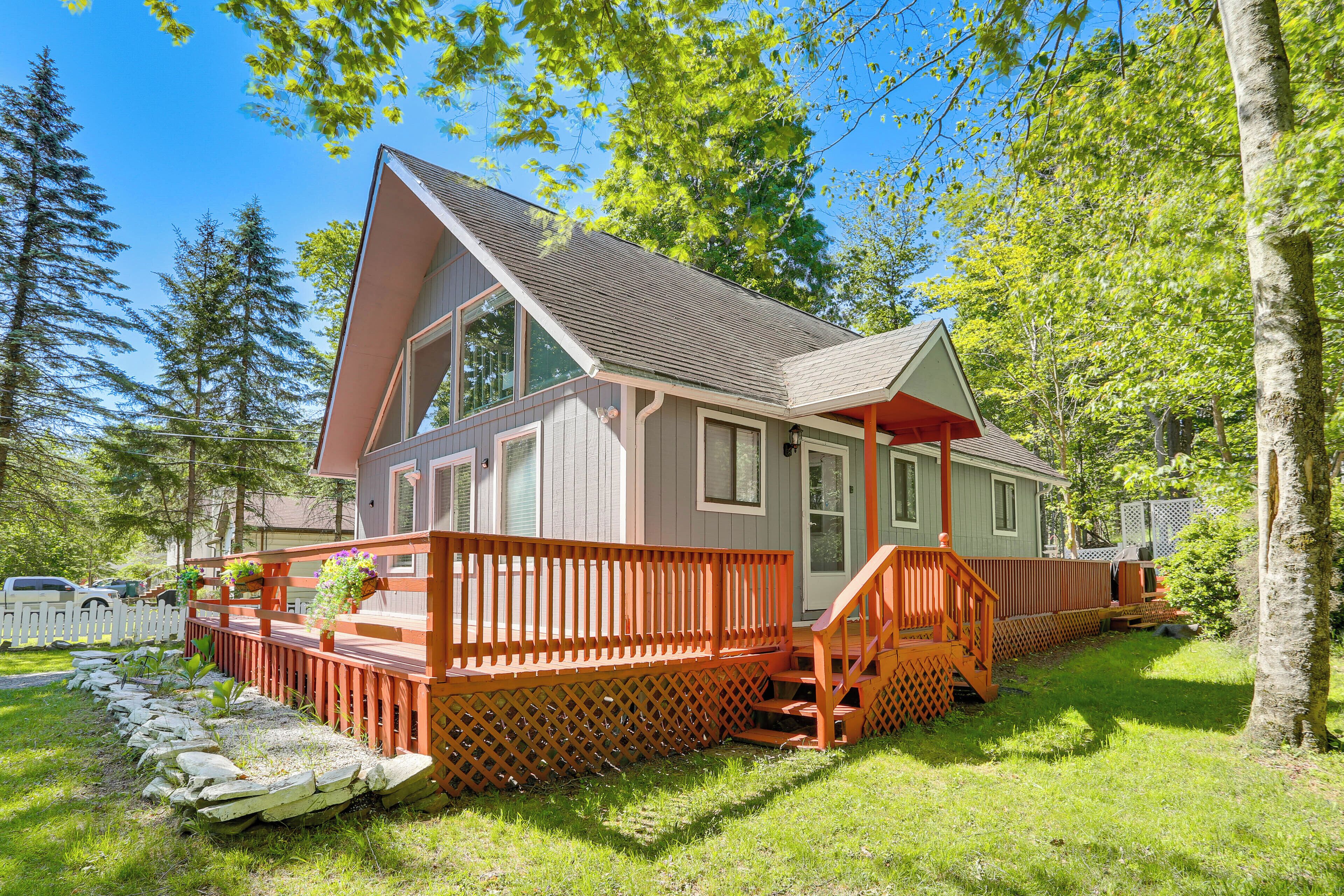 A cabin with a deck, a covered porch, and a stone foundation.