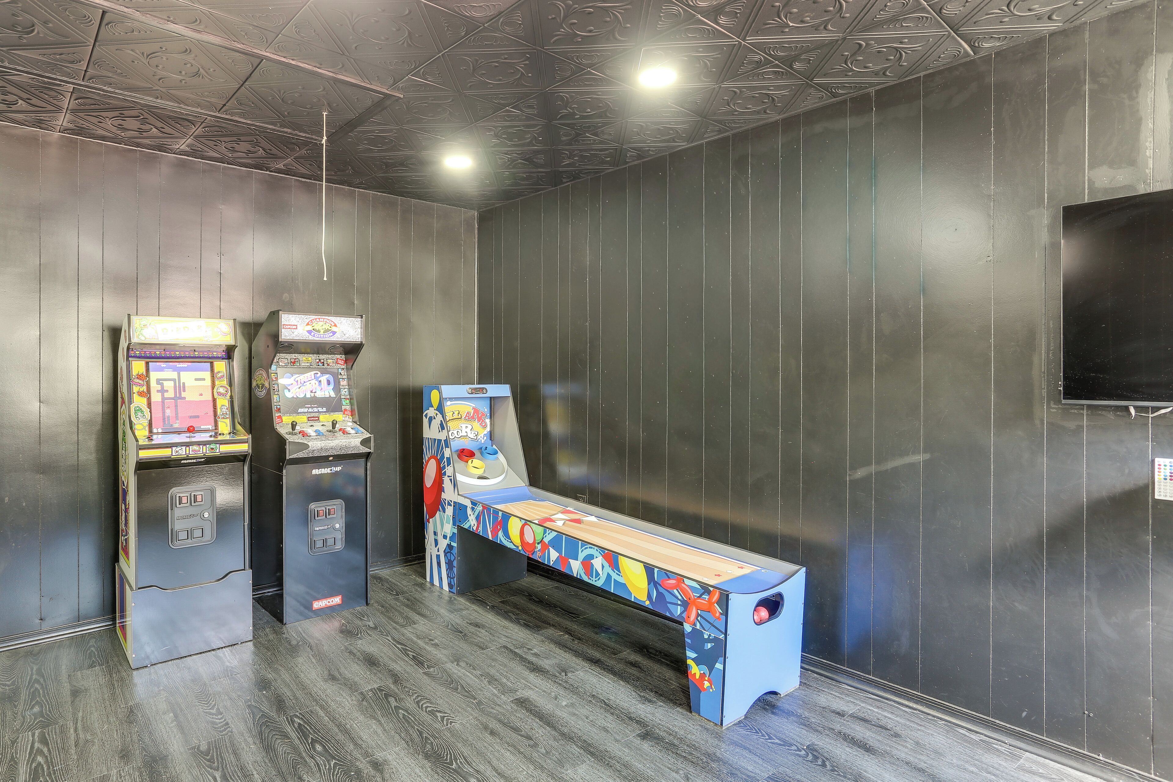 A room with two arcade machines, a bench, and a television on the wall.
