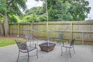 A patio area with metal chairs and a fire pit, surrounded by a wooden fence and trees.