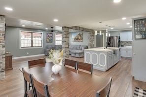 A spacious living area with a dining table, gray sofas, and a kitchen with modern appliances.