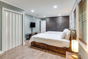 A bedroom with a bed, a TV, a desk, and a window with blinds.