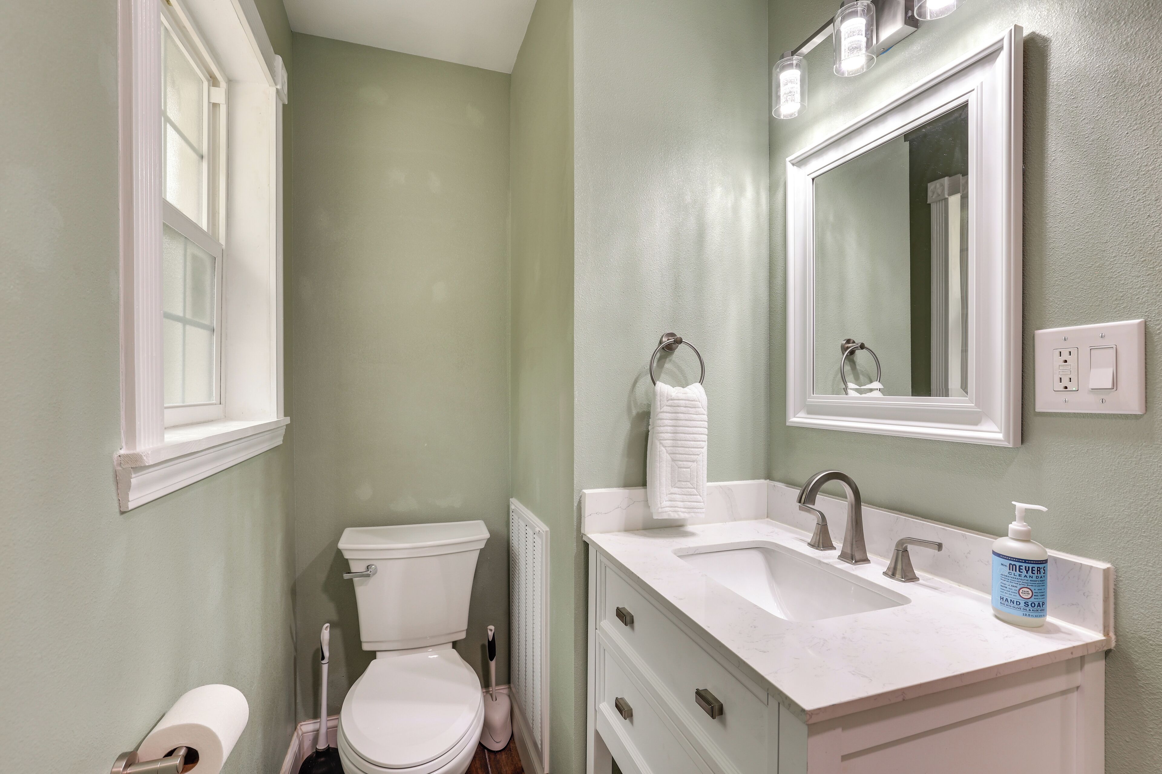 A bathroom with a toilet, sink, mirror, and hand soap.