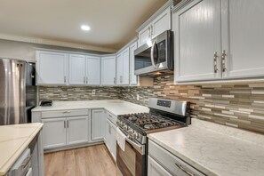 A modern kitchen with white cabinets, a stainless steel refrigerator, a microwave, a stove, and a tiled backsplash.