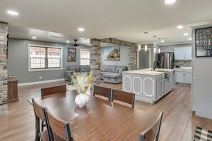 A spacious living area with a dining table, gray sofas, and a kitchen with modern appliances.