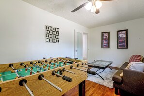 A room with a foosball table, a glass-top table, and a door leading to another room. - Suburban Sanctuary: Magnolia Home w/ Backyard! (Magnolia)
