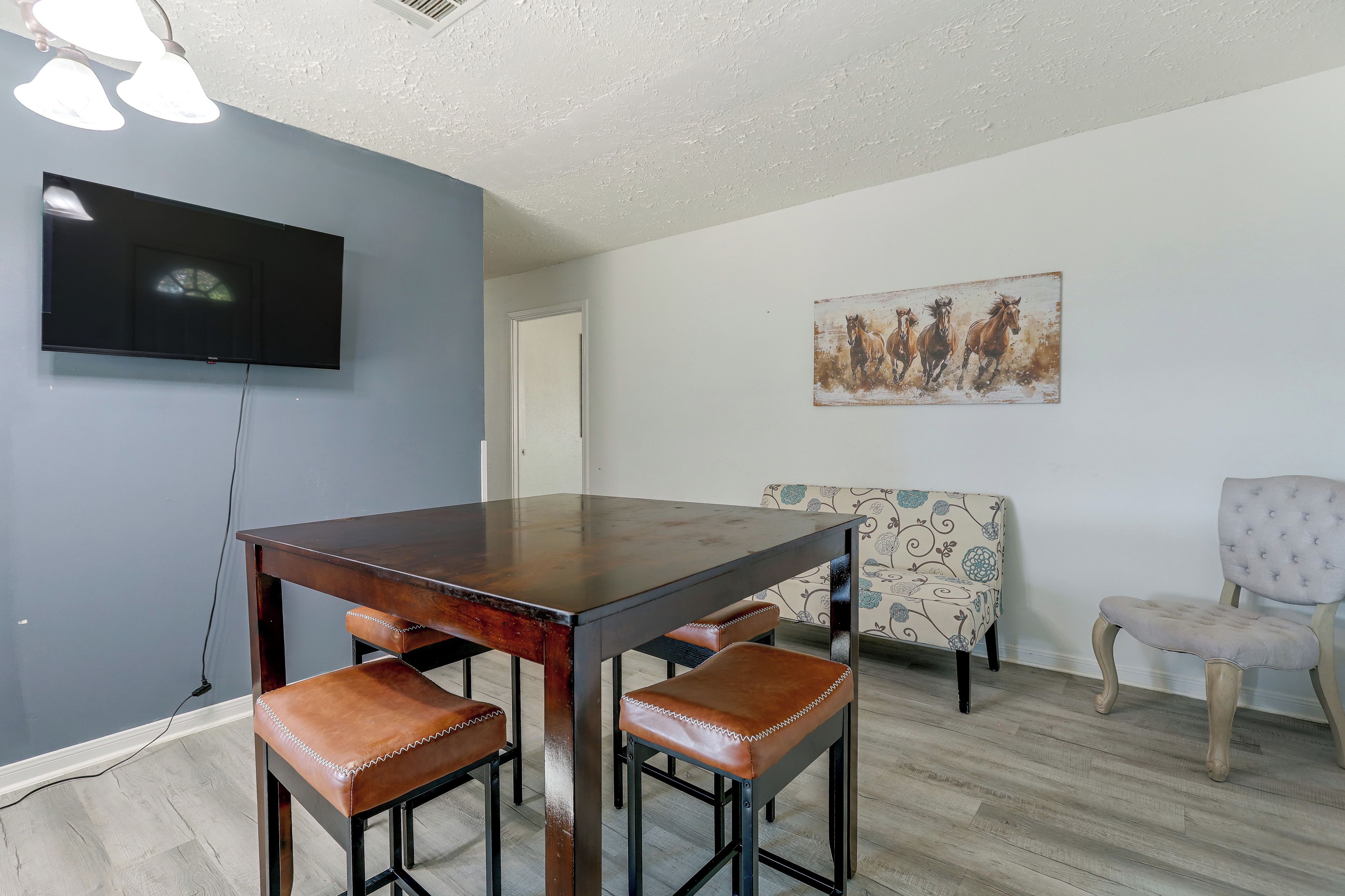 A dining area with a wooden table, two leather chairs, a patterned sofa, and a television mounted on the wall.