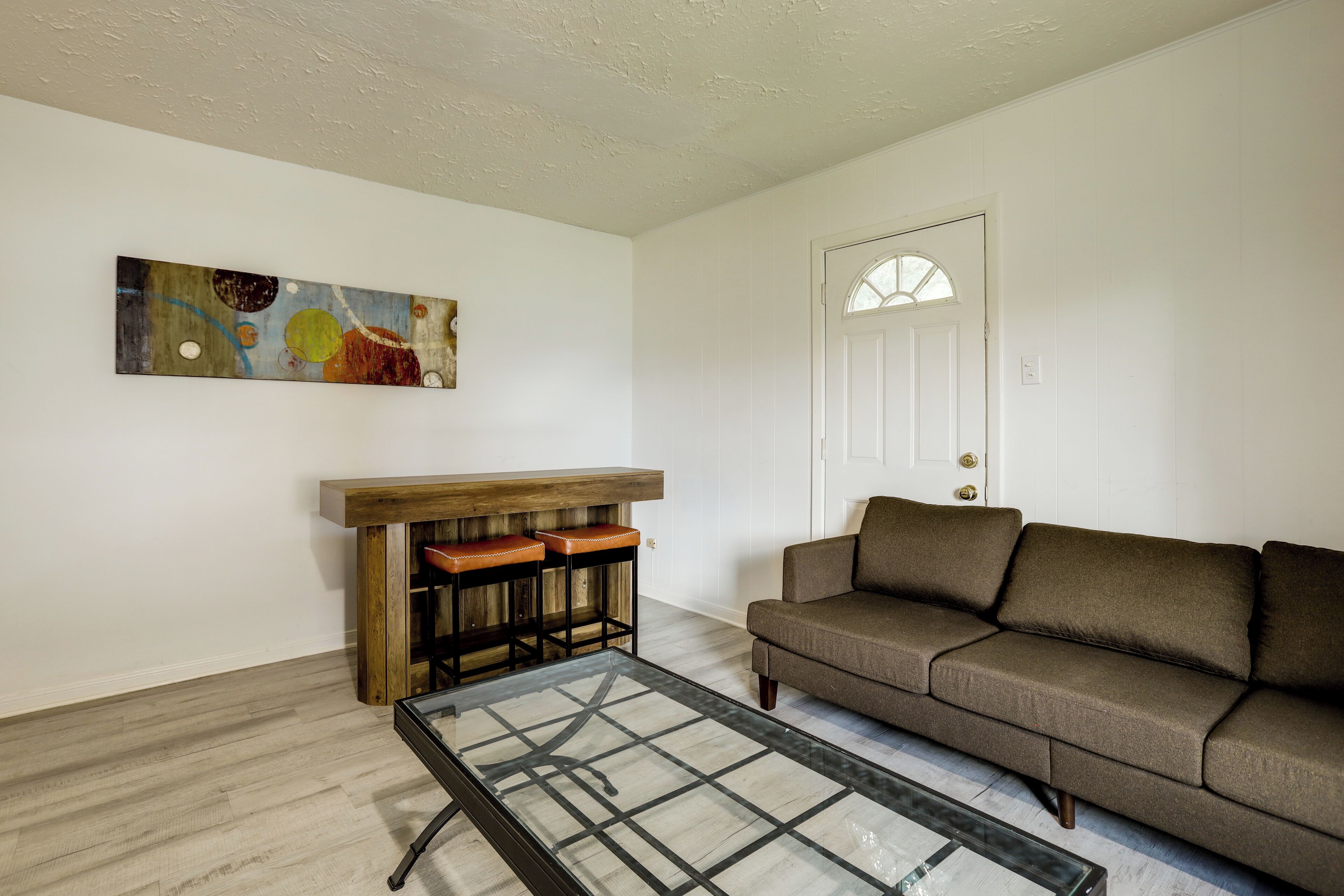 A living room with a wooden bench, a glass coffee table, a brown sofa, and a door with a window.