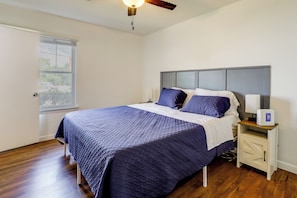 A bedroom with a bed, a nightstand, a ceiling fan, a window, and a door.