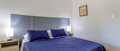 A neatly made bed with a blue quilt, two bedside lamps, a nightstand, and a wall-mounted picture frame.