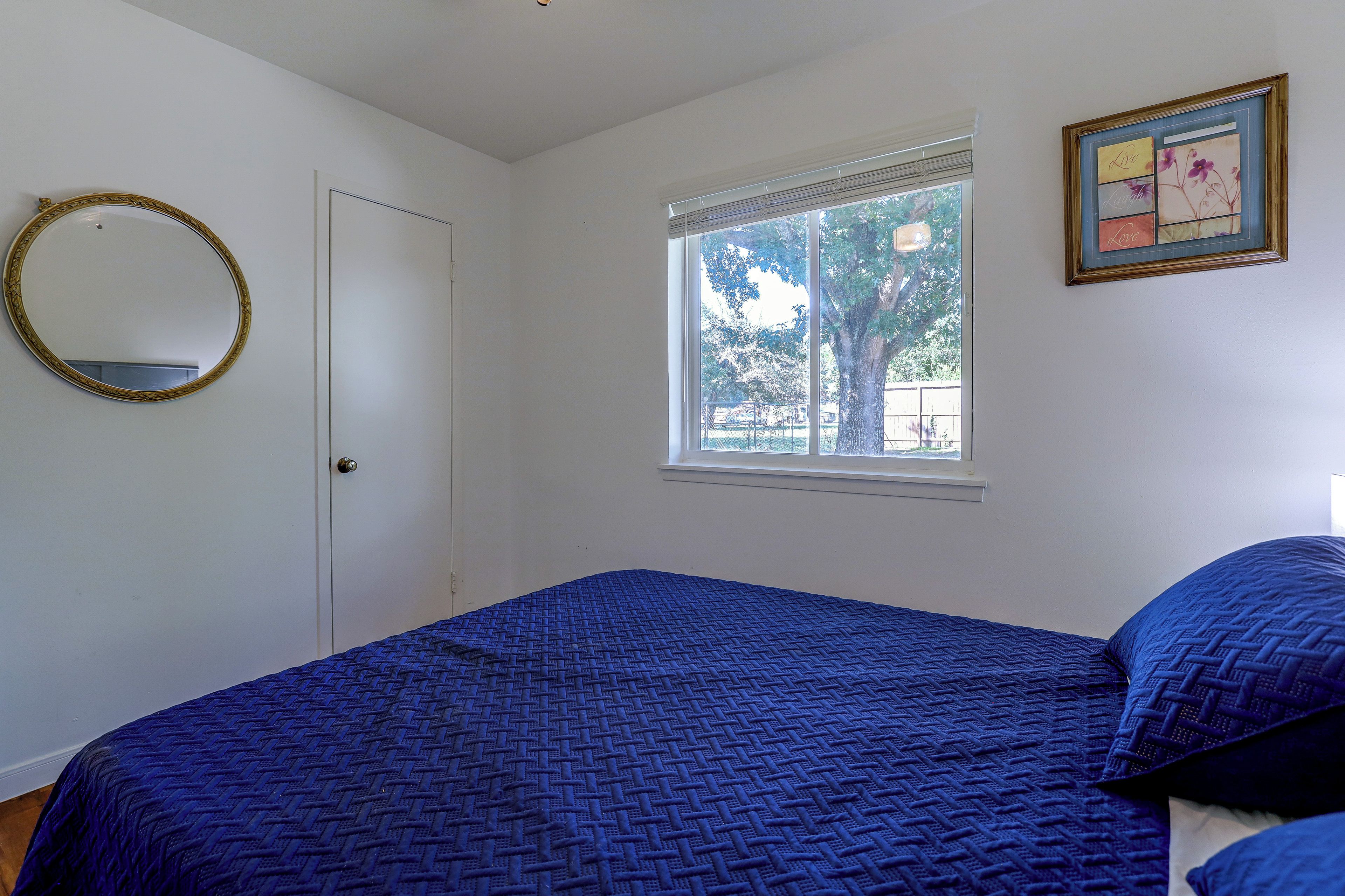 A bedroom with a bed, a window, a door, and a framed picture on the wall.