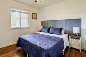 A bedroom with a bed, a nightstand, a bedside table, a window, and a wall-mounted picture.