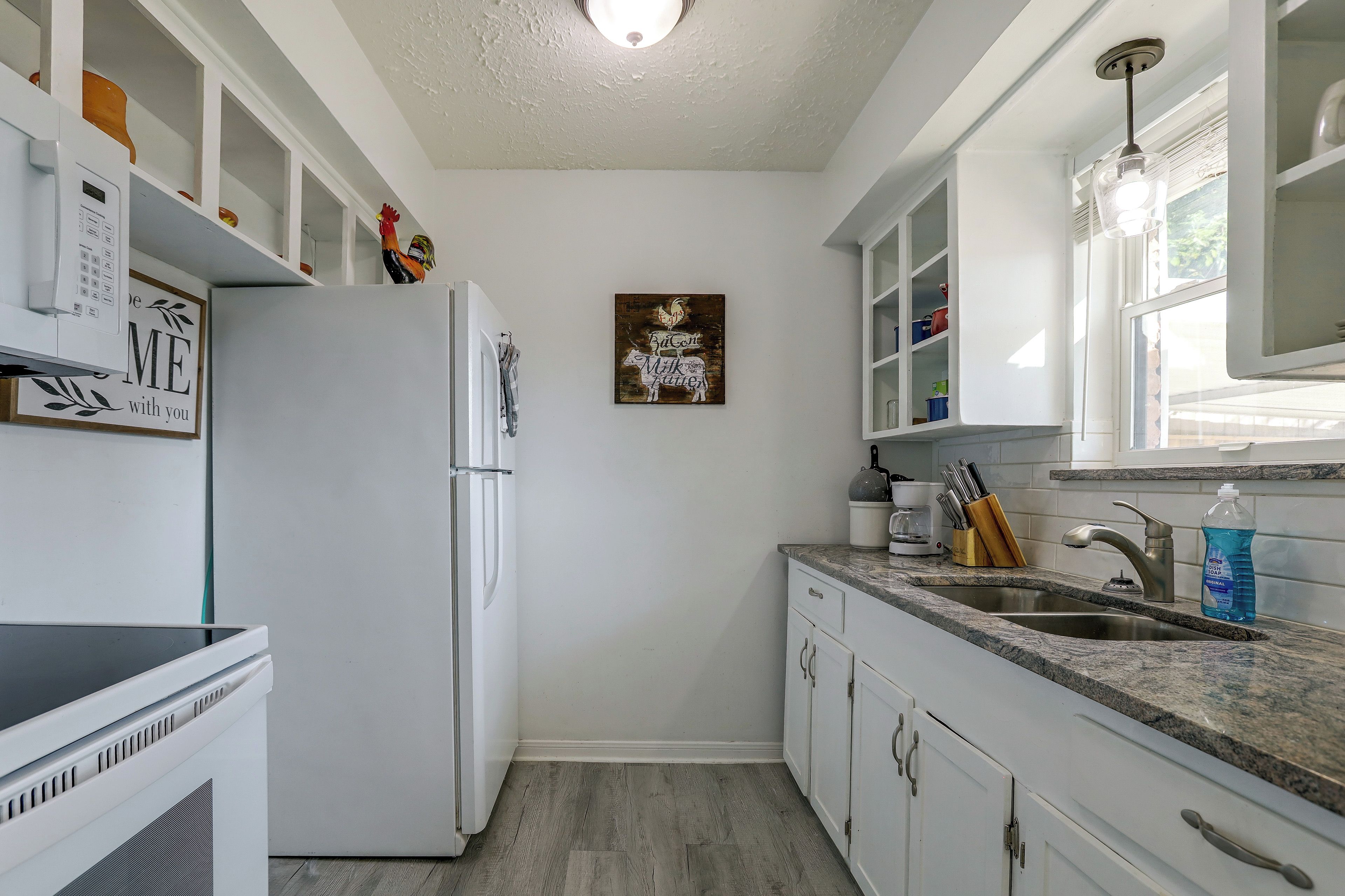A kitchen with white cabinets, a refrigerator, a sink, and a window.