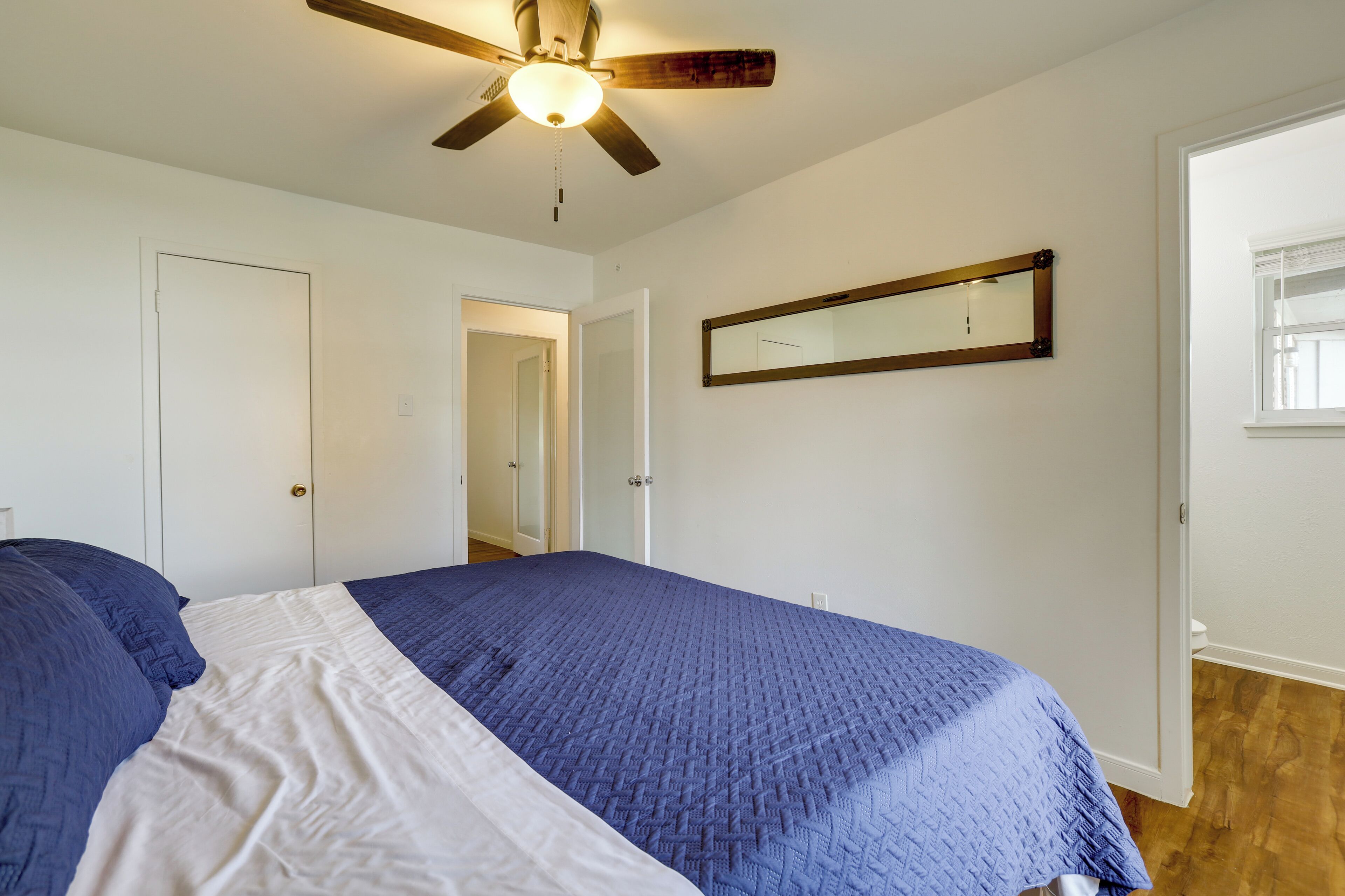 Un dormitorio con cama, ventilador de techo, espejo y puerta.