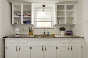 Una cocina con armarios blancos, encimera de granito, un lavabo y una ventana con persianas.