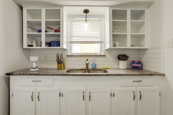 A kitchen with white cabinets, a granite countertop, a sink, and a window with blinds.
