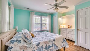 A bedroom with a bed, a ceiling fan, a window with curtains, a dresser, and a door. - Steps to Beach! Emerald Isle Group Escape w/ Yard (Emerald Isle)
