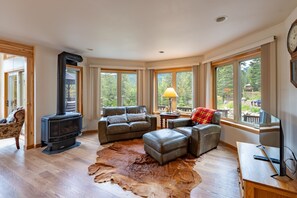 A living room with a fireplace, leather furniture, a large window, and a wooden floor. - Wallowa Lookout: Scenic Retreat w/ Hot Tub (Joseph)