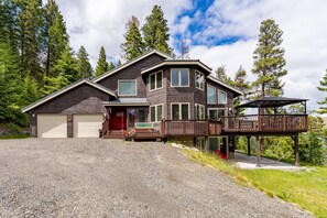 Ein zweistöckiges Haus mit Garage, einer überdachten Veranda und einer Terrasse mit Blick auf eine natürliche Landschaft.