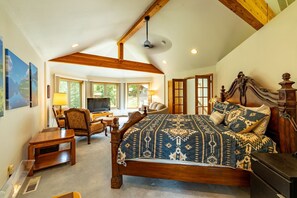 A bedroom with a large bed, wooden ceiling beams, a desk with a chair, and a television. - Wallowa Lookout: Scenic Retreat w/ Hot Tub (Joseph)
