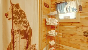 A wooden cabin interior with a metal shelf holding towels, a window with a curtain, and a wall mural. - Near White River Fishing! Studio Cabin w/ Grill (Fifty-Six)