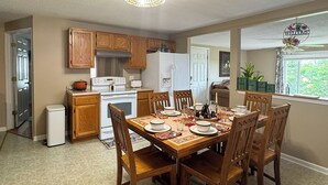 A dining area with a wooden table set for four, surrounded by wooden chairs. A white refrigerator and stove are visible in the background. - Families Welcome! Corinth Escape w/ Lake Views (Corinth)