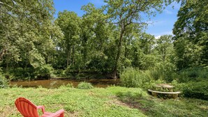 Ein roter Adirondack-Sessel am Ufer eines Teichs, umgeben von dichtem Baumbestand.