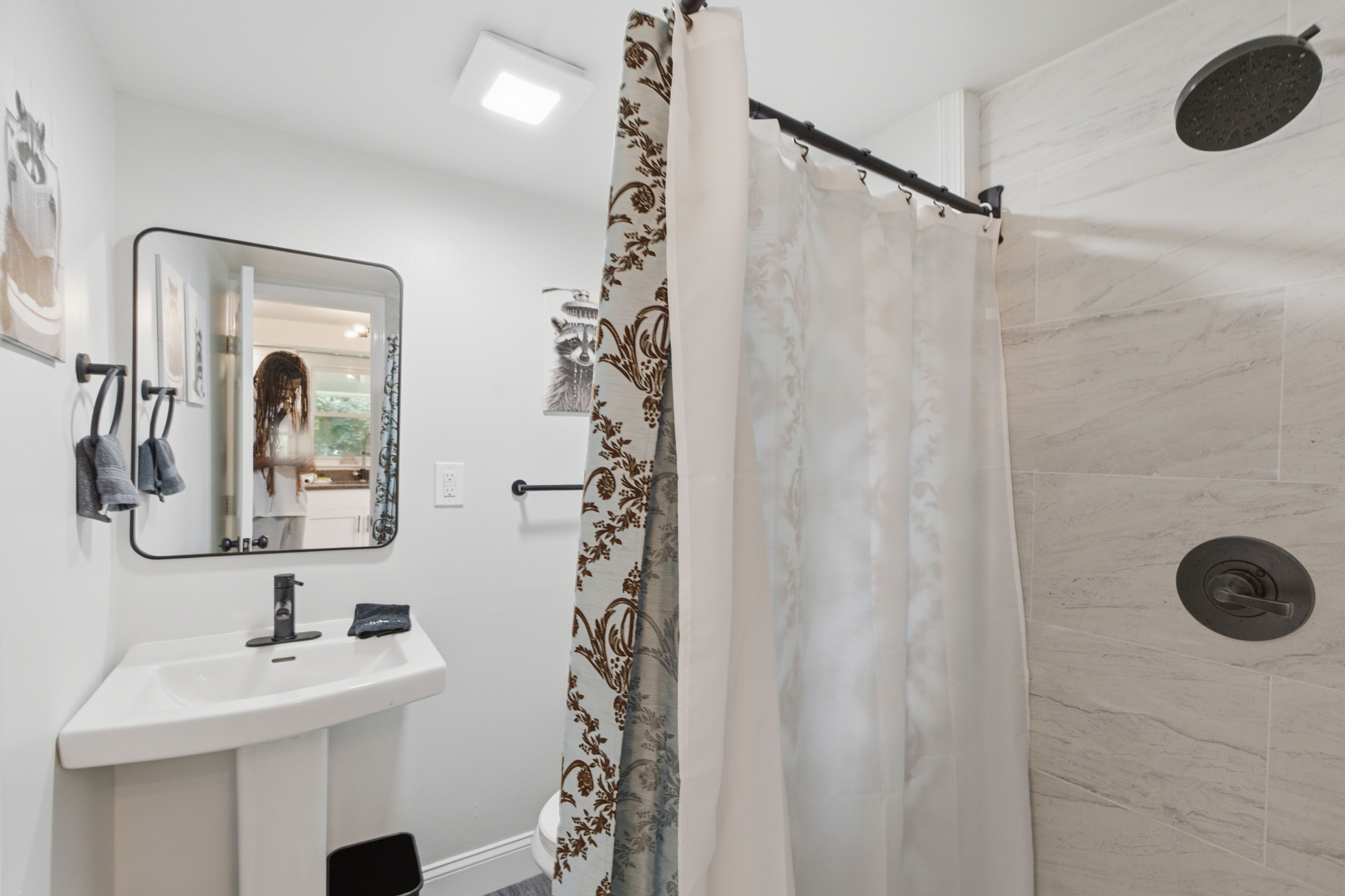 Ein Badezimmer mit Waschbecken, Spiegel, Dusche und einer weißen Vorhang sowie einer gefliesten Wand.