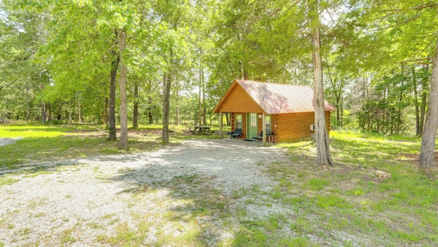 A cabin with a gravel driveway, surrounded by trees.