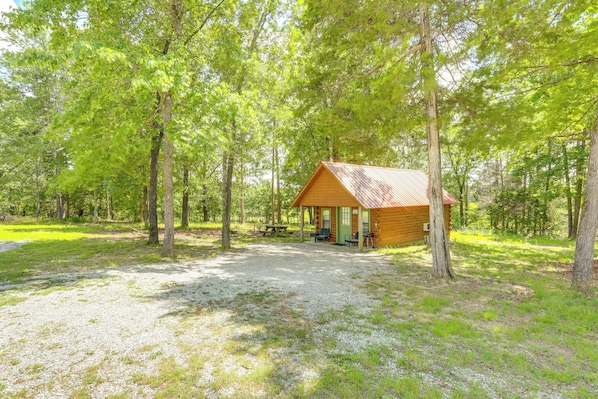 A cabin with a gravel driveway, surrounded by trees.