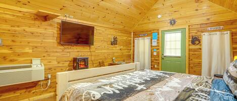 Una habitación de cabaña de madera con una cama, un televisor montado, una puerta verde y un cartel que dice 'WANDER'.