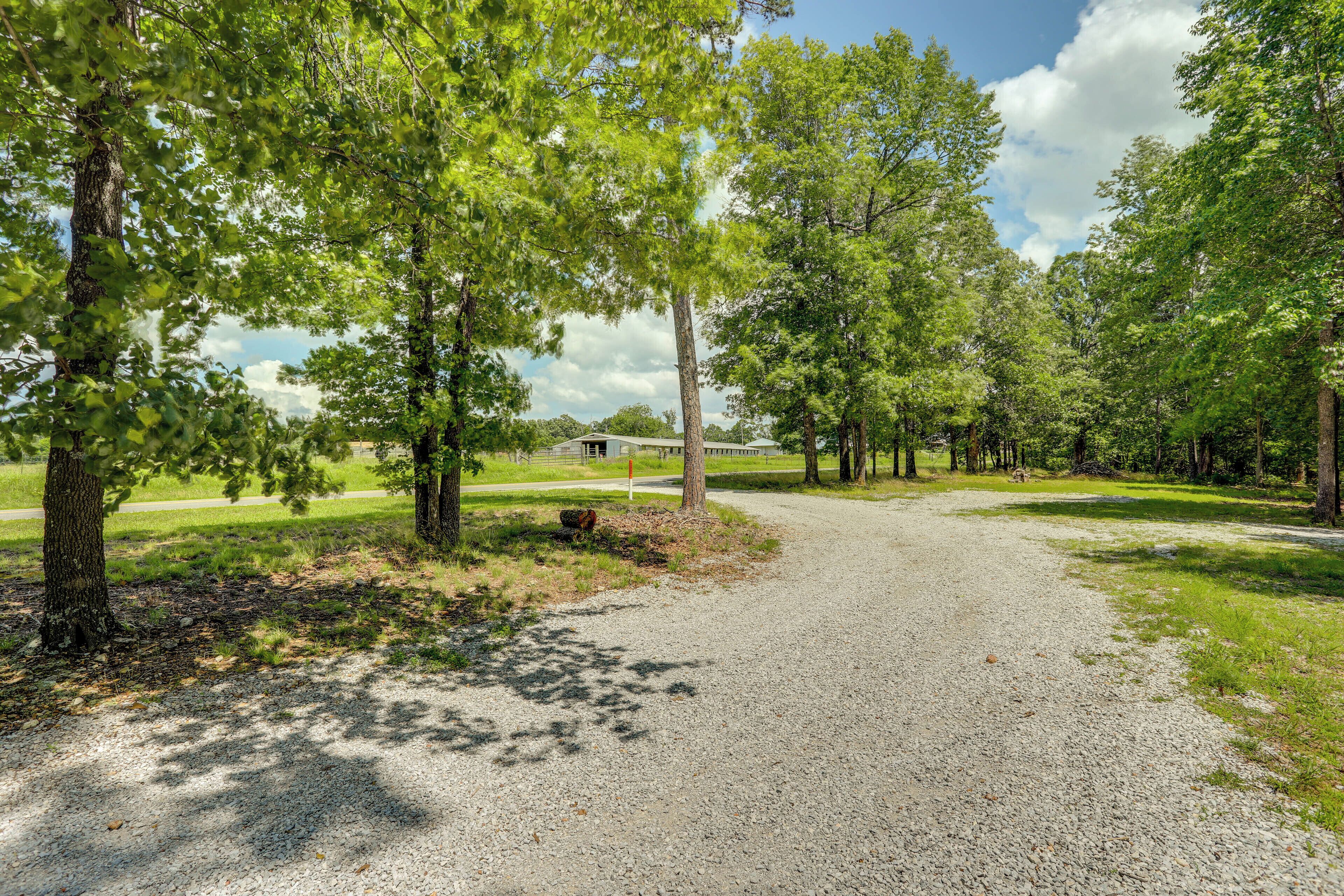 A gravel path leading through a wooded area with trees and a building in the background.