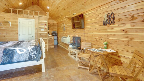 Ein Holzblockhaus-Interieur mit einem Bett, einem Tisch, Stühlen, einem Fernseher und einem Kamin.