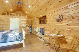 A wooden cabin interior with a bed, a table, chairs, a TV, and a fireplace.