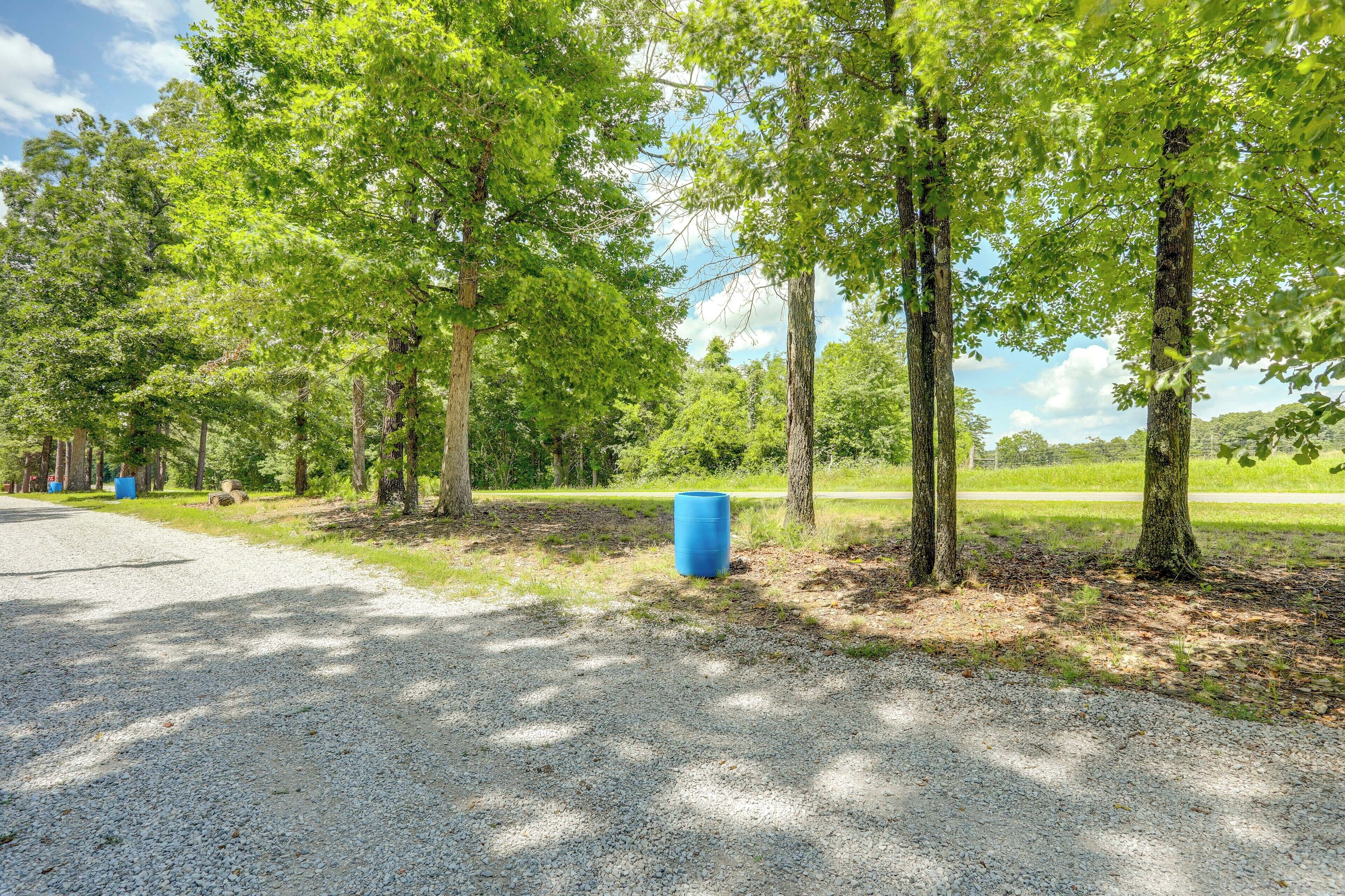A gravel path leading through a wooded area with trees and a blue barrel.