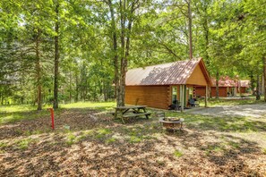 A cabin with a picnic table and fire pit in a forested area.