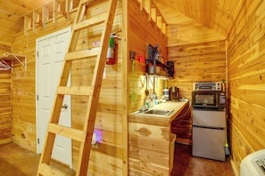 A wooden cabin interior with a kitchen area, including a sink, stove, and refrigerator.