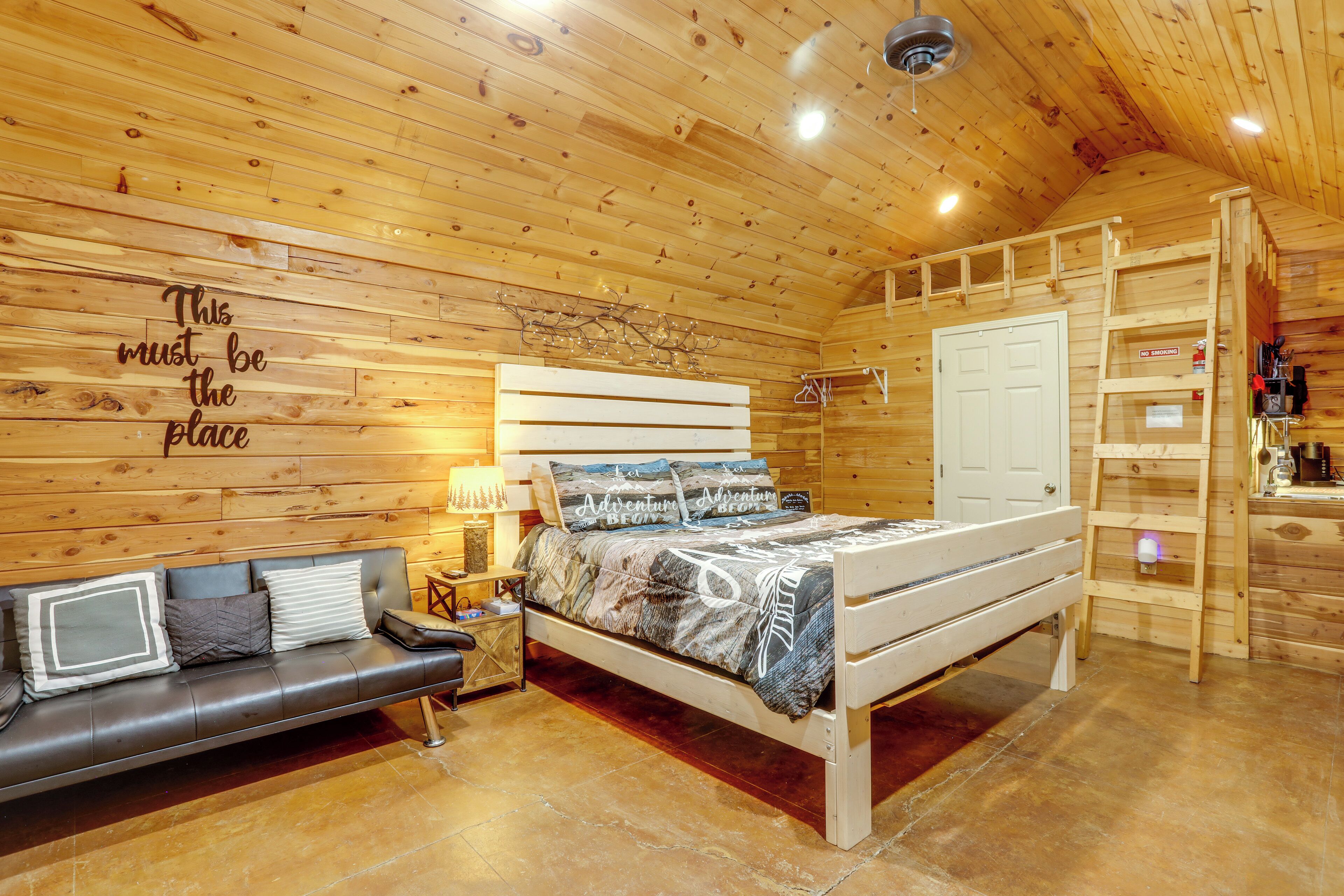 Interior de una cabaña de madera con una cama, un sofá, una escalera y una pared con un letrero.