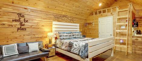 A wooden cabin interior with a bed, a sofa, a ladder, and a wall with a sign.