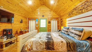 A cozy cabin-style room with a wooden ceiling, a bed with a patterned bedspread, a television, and a small table with a heater.