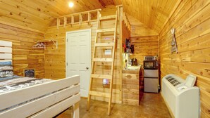 A wooden cabin interior with a bunk bed, a ladder, a kitchenette, and a heater.