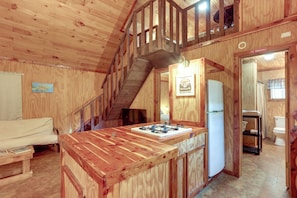 L’intérieur d’une cabane en bois comprend un coin cuisine, une table à manger et un escalier menant à un étage supérieur.